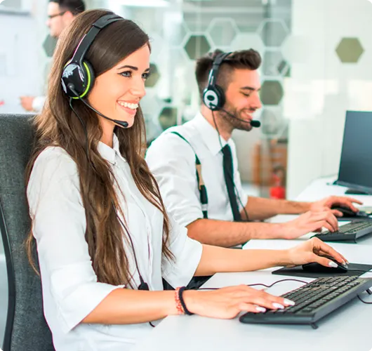 A professional male and female customer support team wearing headsets and working at their computers in a modern office with a honeycomb wall pattern.